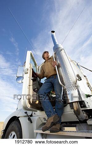 Stock Image - a man standing on the step of the cab of his truck; three hills, alberta, canada. Fotosearch