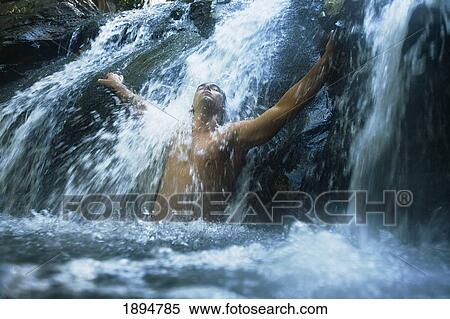 Stock Photography - a man standing under a waterfall with arms outstretched at the currumbin rock pools in currumbin valley; gold coast, queensland, australia. Fotosearch