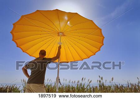 a man standing under an orange sun umbrella looking out to sea; cadiz, andalusia, spain View Large Photo Image Stock Photo - a man standing under an orange sun umbrella looking out to sea; cadiz, andalusia, spain. Fotosearch