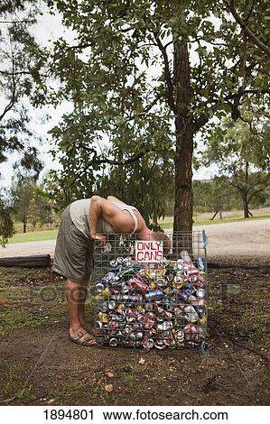 Stock Image - a man sticking his head in a bin filled with empty cans by a sign reading 'only cans'; queensland, australia. Fotosearch