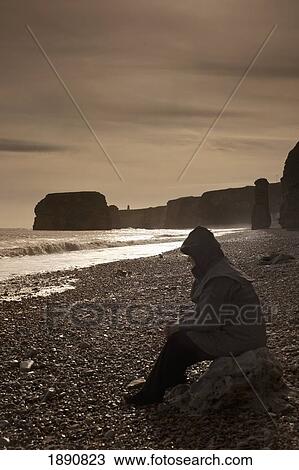 a man wearing a coat and hood sitting on a rock by the shore; south shields, tyne and wear, england View Large Photo Image Stock Image - a man wearing a coat and hood sitting on a rock by the shore; south shields, tyne and wear, england. Fotosearch