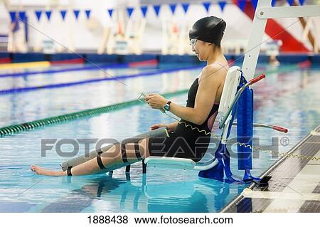 Stock Photo - a paraplegic woman is lowered into the swimming pool on a lift and prepares to swim; edmonton, alberta, canada. Fotosearch
