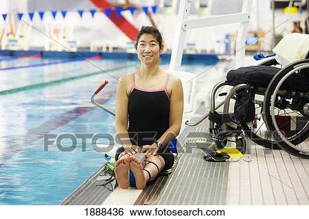 Stock Photograph - a paraplegic woman sits at the edge of a swimming pool on a lift beside her wheelchair and prepares to swim; edmonton, alberta, canada. Fotosearch