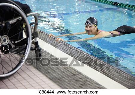 Picture - a paraplegic woman swims in a pool with her wheelchair at the water's edge; edmonton, alberta, canada. Fotosearch