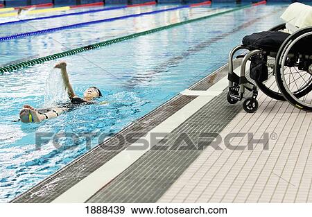 Stock Photo - a paraplegic woman swims in a pool with her wheelchair at the edge of the pool; edmonton, alberta, canada. Fotosearch