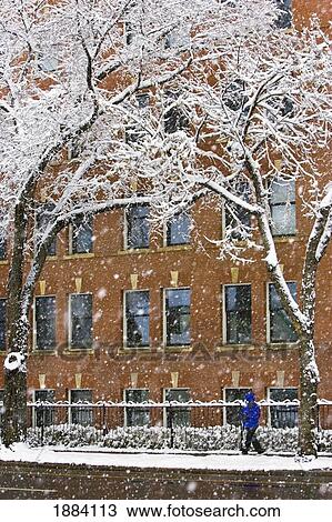 Stock Image - a person dressed in a winter coat walks by an old apartment building as heavy snowflakes fall to the ground; edmonton, alberta, canada. Fotosearch