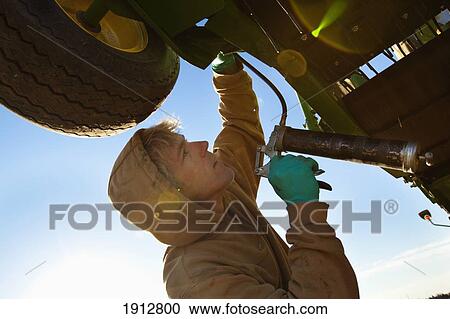 Stock Image - a person works on farm equipment; three hills, alberta, canada. Fotosearch