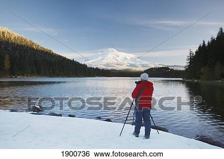Stock Photograph - a photographer uses a camera on a tripod to capture mount hood and trillium lake at sunrise; oregon, united states of america. Fotosearch
