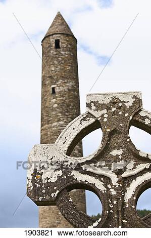 Stock Image - a tombstone in a cemetery and a round tower on a 6th century monastic site; glendalough, county wicklow, ireland. Fotosearch