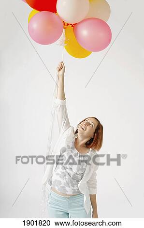 Stock Image - a woman holding a bunch of helium balloons. Fotosearch