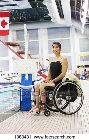Stock Image - a woman in a wheelchair sits beside a lift on the edge of a swimming pool; edmonton, alberta, canada. Fotosearch