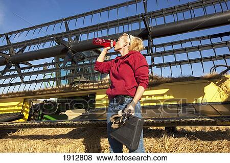 a woman takes a drink as she breaks from work while standing in front of a combine; three hills, alberta, canada View Large Photo Image Stock Photo - a woman takes a drink as she breaks from work while standing in front of a combine; three hills, alberta, canada. Fotosearch