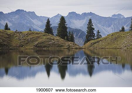 Stock Photo - alpine lake reflecting a mountain range and trees; oberstdorf, germany. Fotosearch