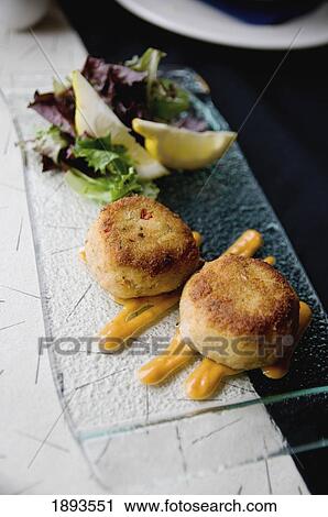 Stock Image - fried crab cakes and salad with two lemon wedges on a plate; tofino, british columbia, canada. Fotosearch