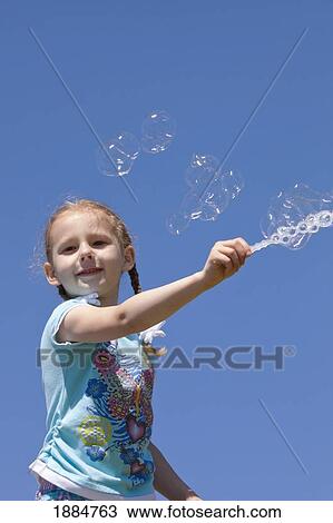 Stock Image - girl playing with bubbles against a blue sky; portland, oregon, united states of america. Fotosearch