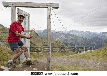 male hiker on top of a mountain stepping into an open wooden door and frame overlooking a mountain valley, lake and mountain range; oberstdorf, germany View Large Photo Image Stock Image - male hiker on top of a mountain stepping into an open wooden door and frame overlooking a mountain valley, lake and mountain range; oberstdorf, germany. Fotosearch