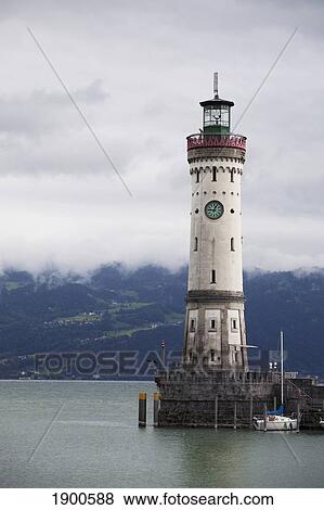 Stock Photo - old lighthouse on a pier of a lake with cloud covered mountains in the background; lindau, germany. Fotosearch