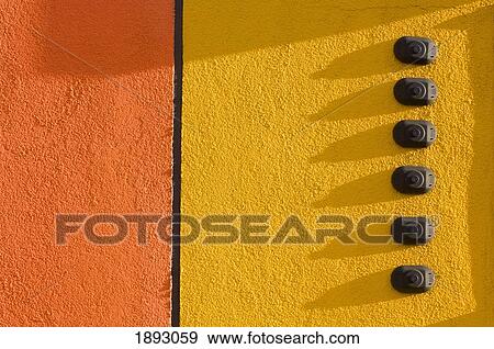 Stock Photo - orange and yellow stucco wall with 6 doorbells; st. albert, alberta, canada. Fotosearch