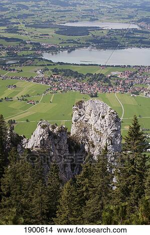 Picture - rock cliffs with trees overlooking a lake and village; fussen, germany. Fotosearch
