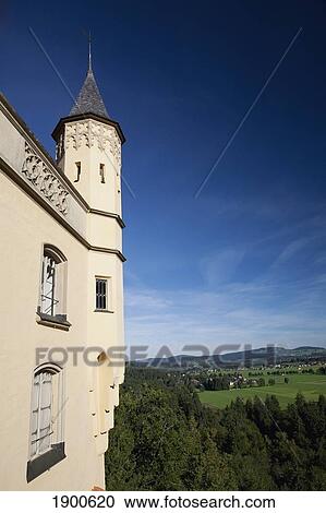 Stock Image - side wall and turret of a bavarian castle on a mountain side with fields and a village in the background; fussen, germany. Fotosearch