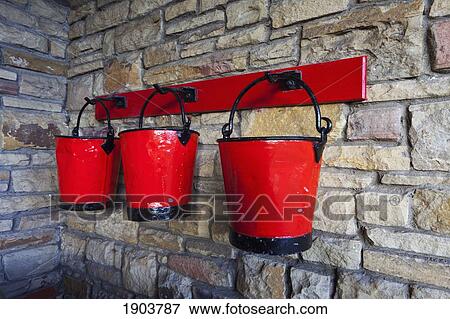 Stock Photo - three red pails hanging in a row on hooks on a stone wall; beamish, durham, england. Fotosearch