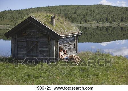 Stock Photography - two girls resting again a wooden shed by the lake; vang, norway. Fotosearch
