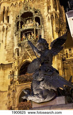 Stock Photography - winged statue with a lit city hall tower and glockenspiel in the background at night; munich, germany. Fotosearch