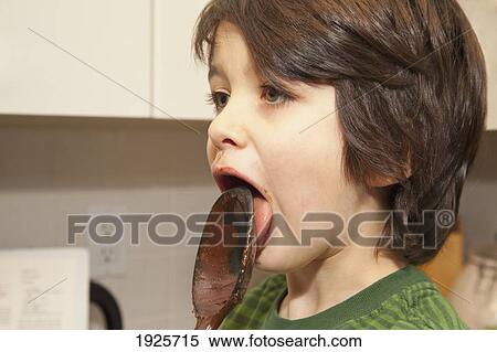Stock Photography - a boy licking a spoon with chocolate on it; langley, british columbia, canada. Fotosearch