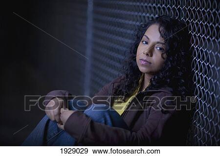 Stock Photo - a girl sits alone in the dark along a chain link fence; edmonton, alberta, canada. Fotosearch