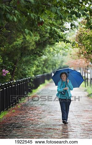 Stock Photography - a woman walking down a path holding an umbrella in the rain; tokyo, japan. Fotosearch