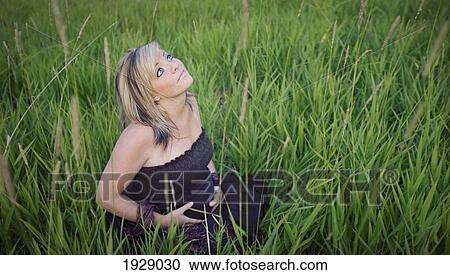 Stock Image - a young woman sits in tall grass with her hands on her pregnant belly; edmonton, alberta, canada. Fotosearch