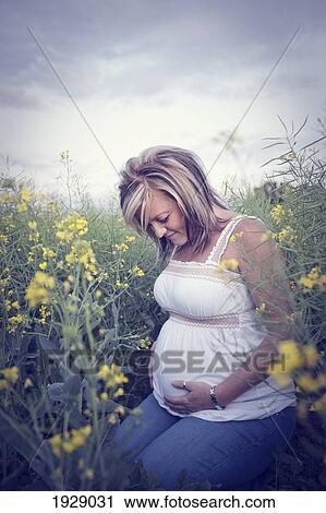 a young woman sits in the wildflowers with her hands on her pregnant belly; edmonton, alberta, canada View Large Photo Image Stock Image - a young woman sits in the wildflowers with her hands on her pregnant belly; edmonton, alberta, canada. Fotosearch