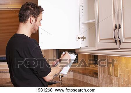 Stock Photo - carpenter measuring and installing new kitchen cabinets. Fotosearch