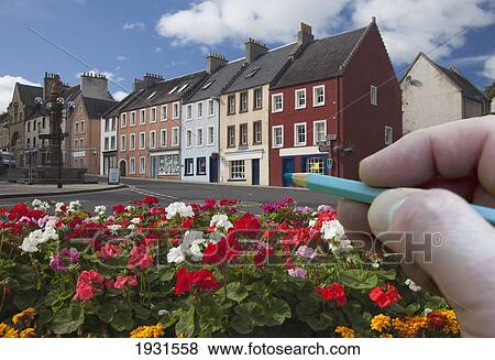 Stock Photo - digitally enhanced image of hand holding pencil against town; jedburgh, scottish borders, scotland. Fotosearch