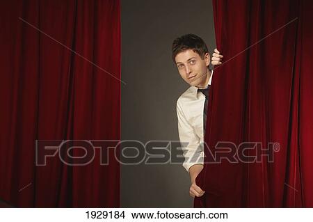 Picture - man peeking from behind a red stage curtain. Fotosearch