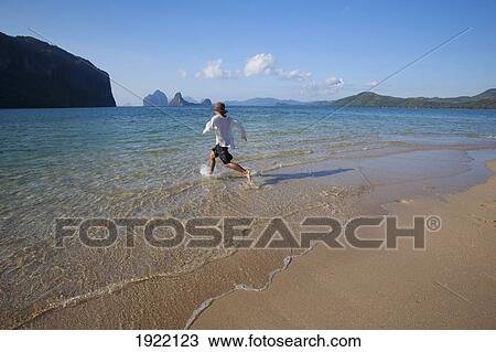Stock Image - man wading into the water; bacuit archipelago, palawan, philippines. Fotosearch