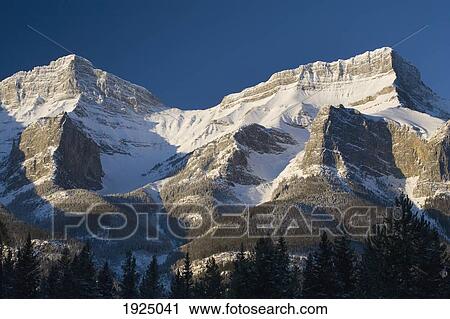 Stock Image - snow capped mountain range against a deep blue sky; canmore, alberta, canada. Fotosearch
