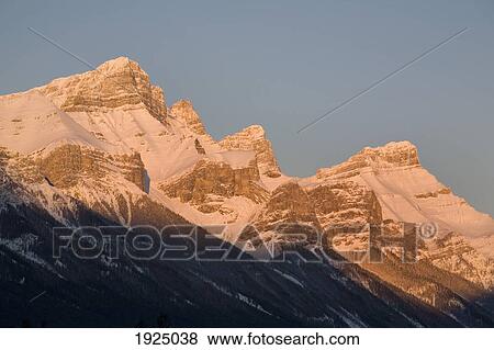 Stock Photo - sunlight shining on snow covered mountains against a blue sky; canmore, alberta, canada. Fotosearch