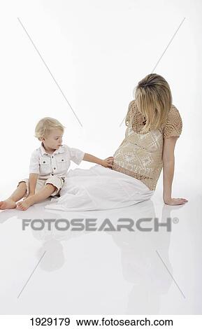 Stock Photo - toddler feeling mother's pregnant stomach on a white background. Fotosearch