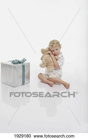 toddler holding a teddy bear sitting beside a wrapped gift View Large Photo Image Stock Image - toddler holding a teddy bear sitting beside a wrapped gift. Fotosearch