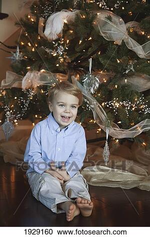 Stock Image - toddler sitting beside christmas tree. Fotosearch