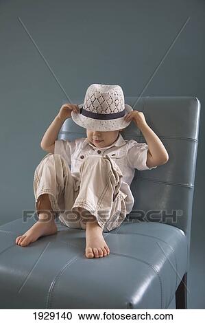 Stock Image - toddler sitting in a big chair wearing a hat; jordan, ontario, canada. Fotosearch