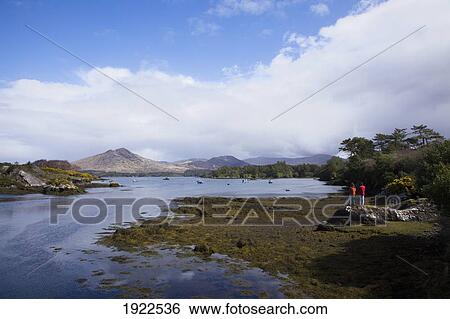 Stock Photograph - two people on the shore looking out over the water; lauragh, county kerry, ireland. Fotosearch