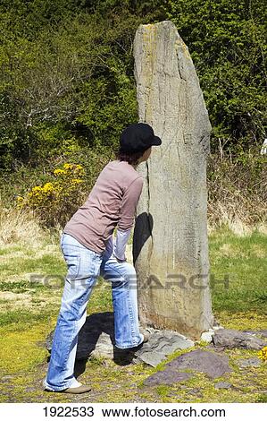 Stock Image - woman looking at ogham stone; caherdaniel, county kerry, ireland. Fotosearch