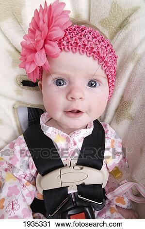 Stock Image - A Baby Girl Sitting In Her Car Seat Wearing A Pink Hat; Alberta, Canada. Fotosearch