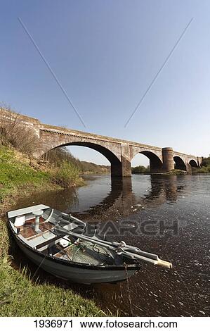 A Boat Left At The Shore By A Bridge In River Tweed; Northumberland England View Large Photo Image Stock Image - A Boat Left At The Shore By A Bridge In River Tweed; Northumberland England. Fotosearch