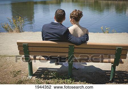 Stock Image - a bride and groom sitting on a bench looking at a lake; oakland california united states of america. Fotosearch
