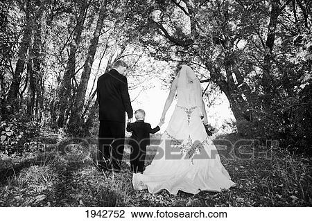 Stock Image - A Bride And Groom Walking And Holding A Young Boy's Hand In Between Them; Edmonton Alberta Canada. Fotosearch
