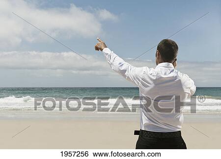 a businessman on the beach talking on his cell phone and pointing to the sky; tarifa cadiz andalusia spain View Large Photo Image Stock Photograph - a businessman on the beach talking on his cell phone and pointing to the sky; tarifa cadiz andalusia spain. Fotosearch