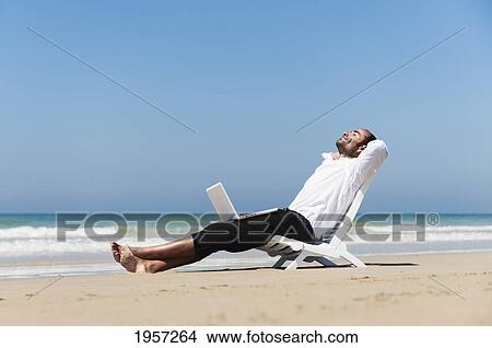 a businessman sits on a beach chair on the beach holding a laptop computer on his lap; tarifa cadiz andalusia spain View Large Photo Image Picture - a businessman sits on a beach chair on the beach holding a laptop computer on his lap; tarifa cadiz andalusia spain. Fotosearch